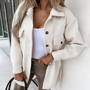 Person wearing a white coat over a white top and beige pants, standing indoors.