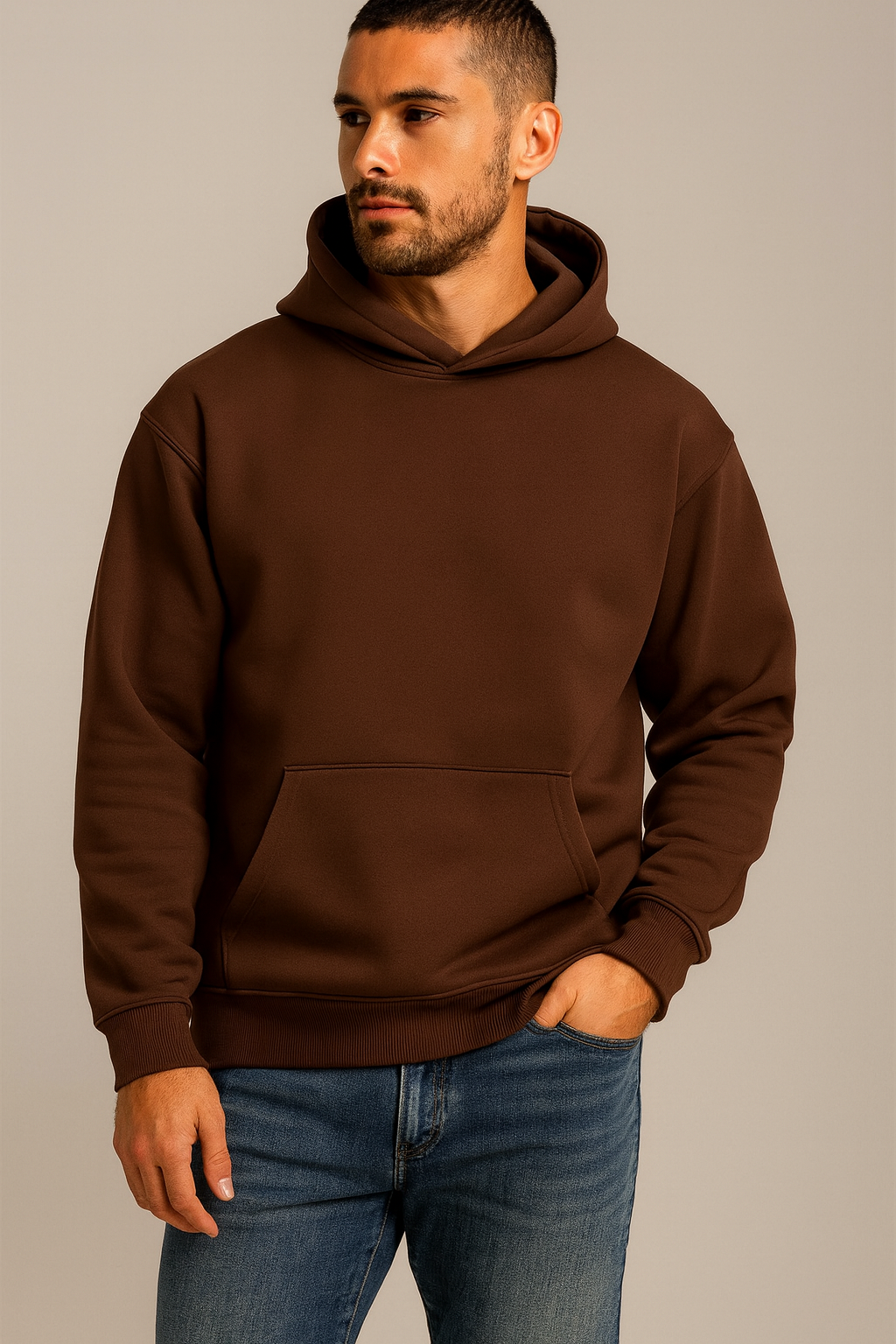 Man wearing a brown hoodie and blue jeans against a neutral background