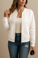 Woman wearing a white bomber jacket over a beige top and blue jeans, holding a black object.