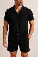 Man wearing A two-piece summer set consisting of a short-sleeved button-up shirt and matching shorts in black color.