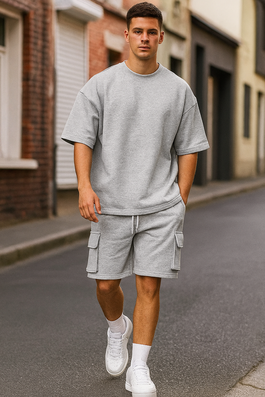 Man wearing a gray oversized t-shirt and cargo shorts with white sneakers on a street.