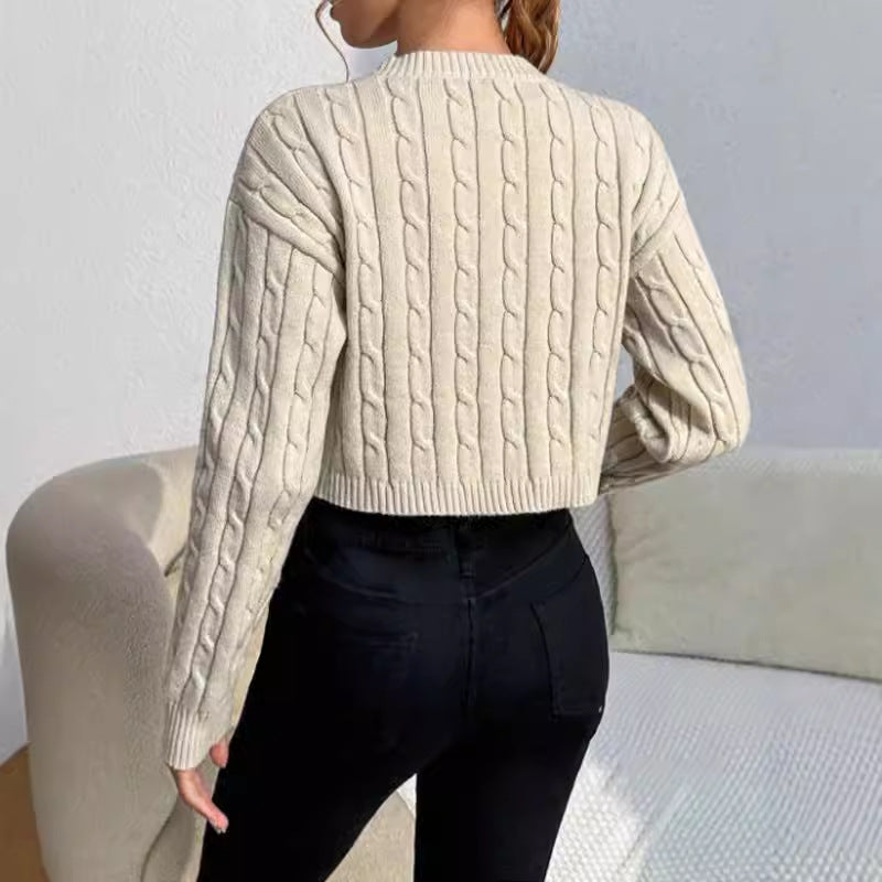 Person wearing a beige cable knit sweater and black pants sitting on a couch.