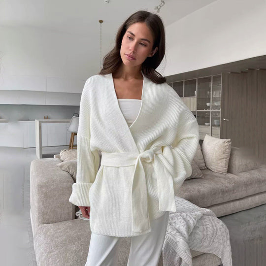 Woman wearing a cream ribbed knit cardigan with a belt in a modern living room