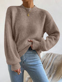 Person wearing a beige sweater and blue jeans against a neutral background