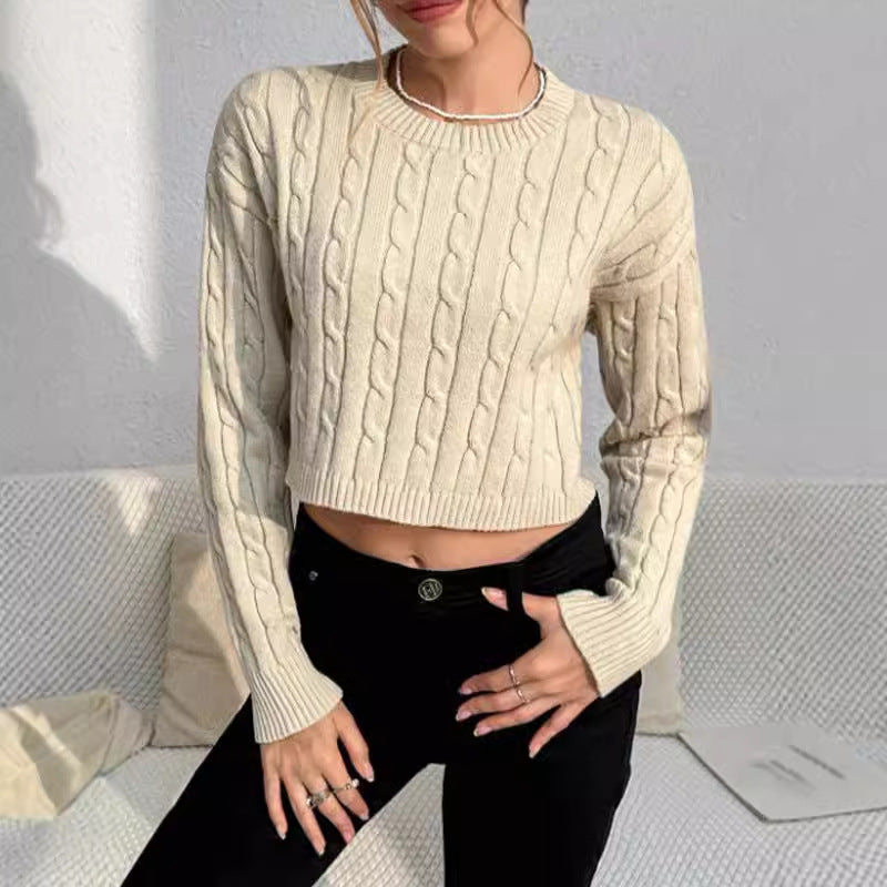 Person wearing a beige cable knit sweater and black pants against a light gray background
