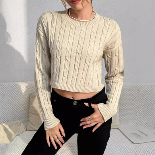 Person wearing a beige cable knit sweater and black pants against a light gray background