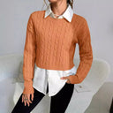 Person wearing a brown cable knit sweater over a white shirt with a plain background
