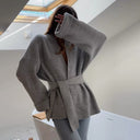 Person wearing a gray belted coat in a modern indoor setting