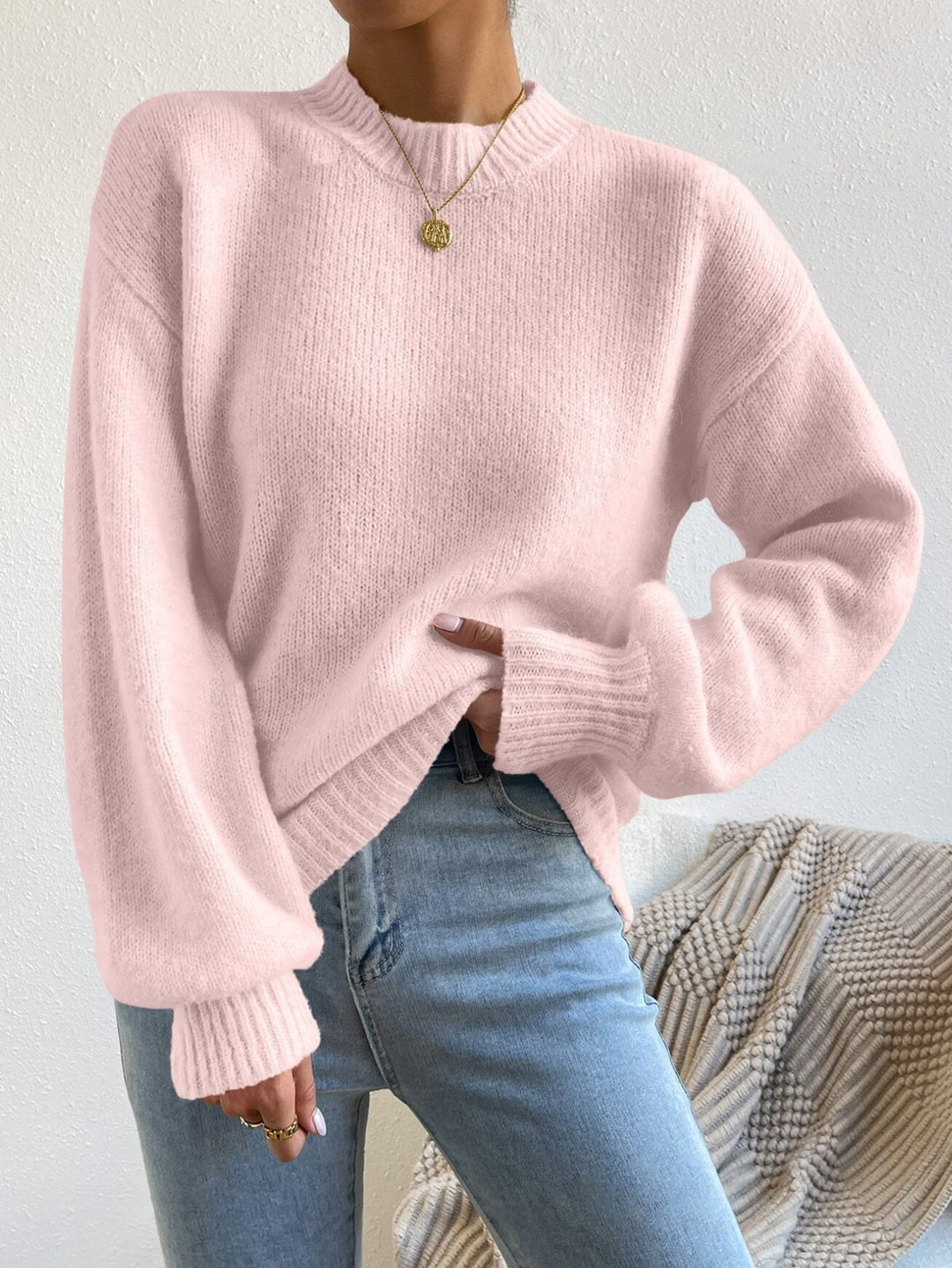 Person wearing a pink sweater and blue jeans against a neutral background