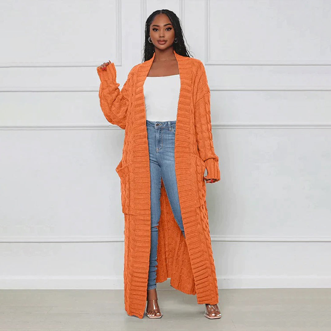 Woman wearing an orange long cardigan, white top, and blue jeans against a white background