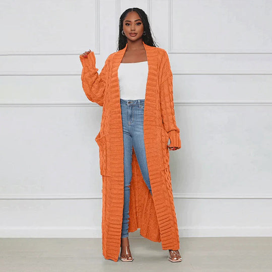 Woman wearing an orange long cardigan, white top, and blue jeans against a white background