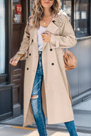 Woman wearing a beige trench coat and blue jeans, standing on a street.