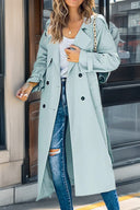 Person wearing a light blue trench coat and ripped jeans standing on a street.