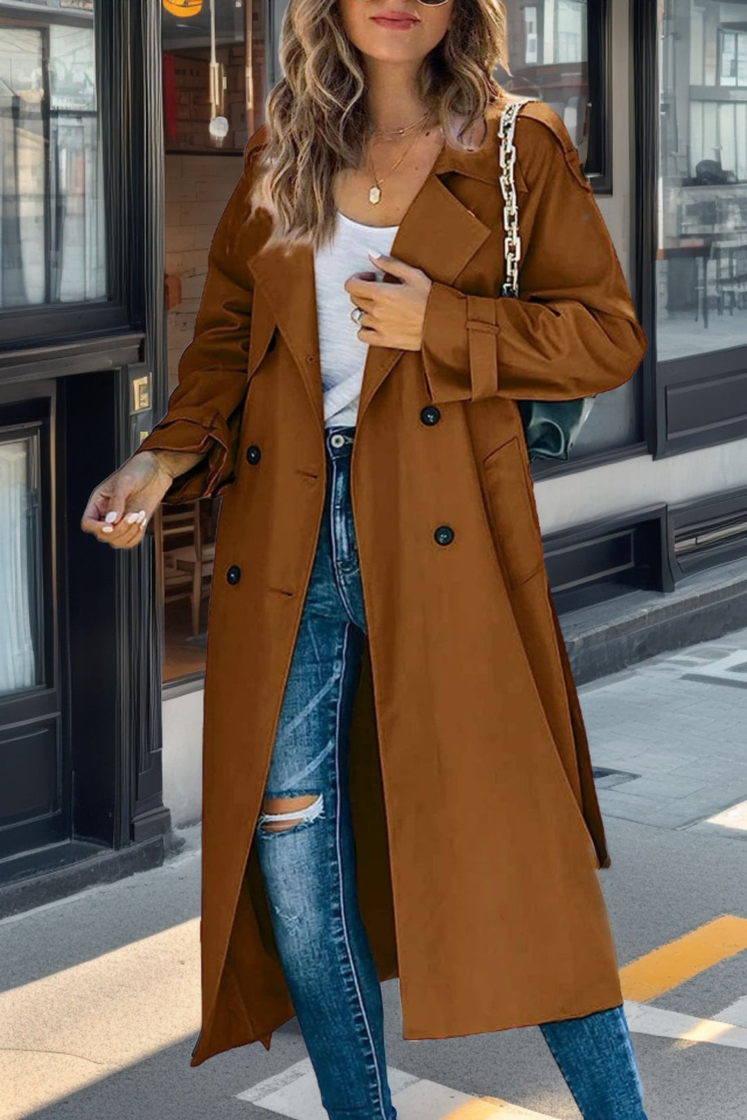 Woman wearing a brown trench coat and ripped jeans on a city street.
