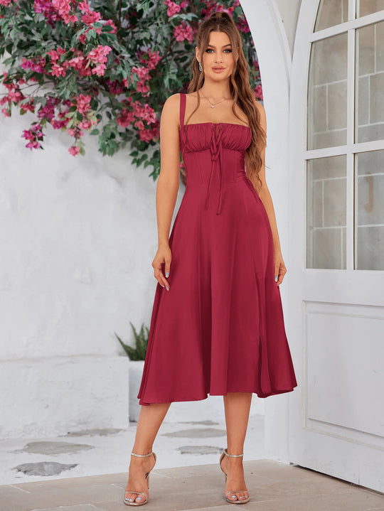 Woman in a burgundy dress standing outdoors with flowers and a white door in the background