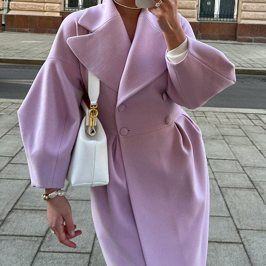 Person wearing a pink coat holding a white handbag on a sidewalk.
