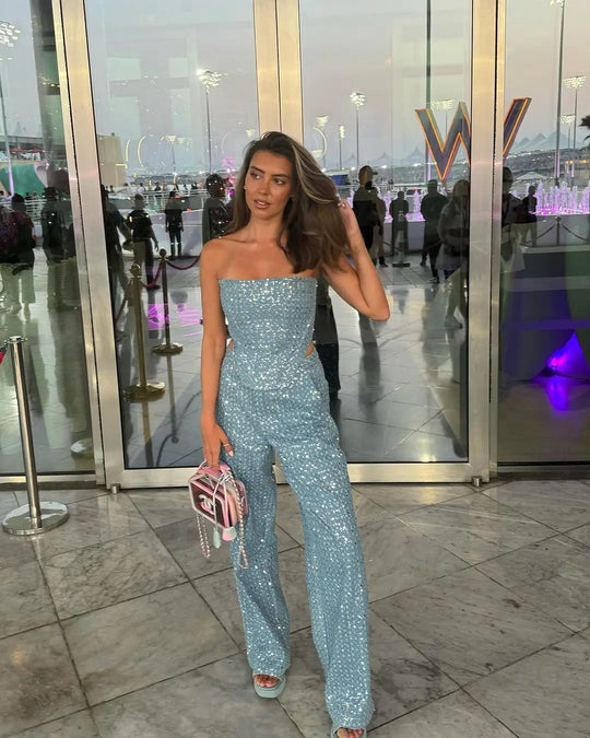 Woman in a sparkly blue jumpsuit standing in front of a glass door with reflections.