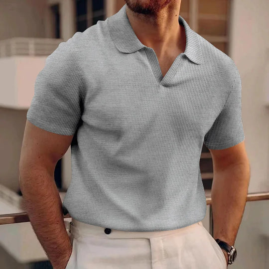 Man wearing a gray polo shirt and light-colored pants in an indoor setting