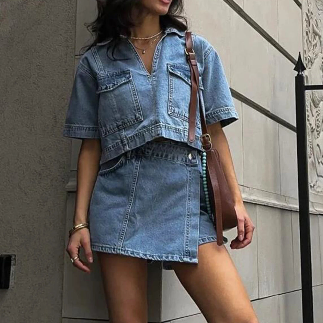 Woman wearing a denim outfit with a matching skirt and top against a neutral wall.