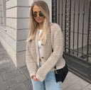 Woman wearing a beige cardigan, white top, and light blue jeans standing on a sidewalk.