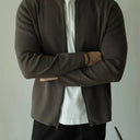 Person wearing a green vest over a white shirt with arms crossed against a plain background