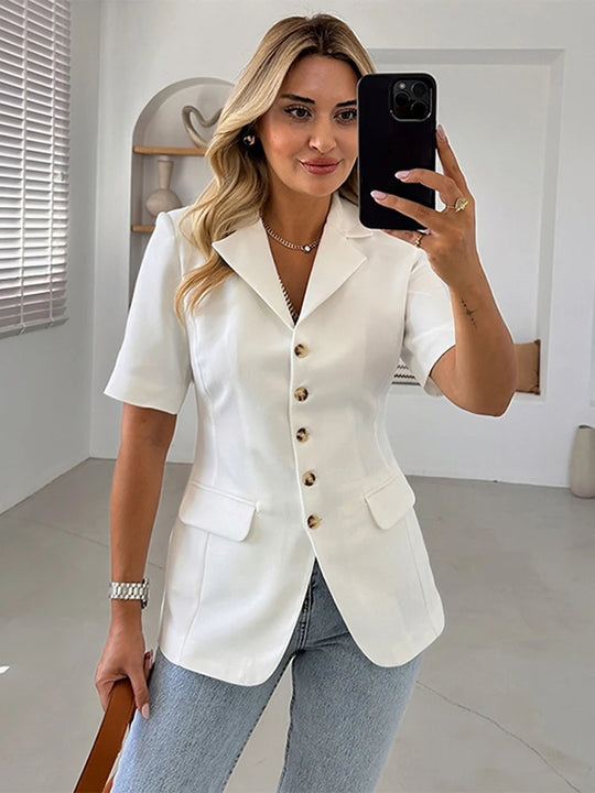 Woman taking a mirror selfie wearing a white blazer and blue jeans indoors.