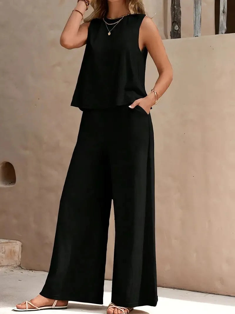 Person wearing a black sleeveless top and wide-leg pants against a beige wall.