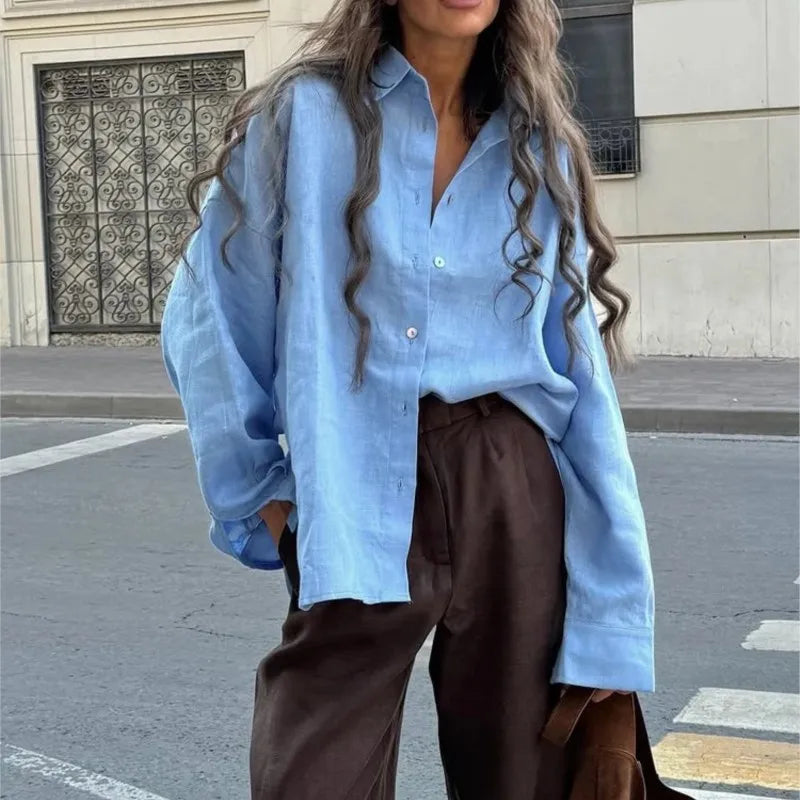 Person wearing a light blue shirt and brown pants on a city street.