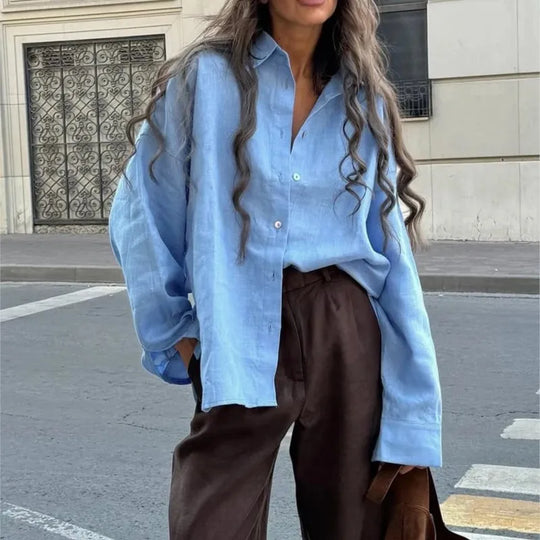Person wearing a light blue shirt and brown pants on a city street.