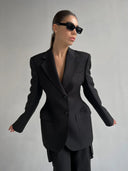 Person wearing a black suit and sunglasses on a gray background