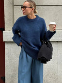 Woman in a blue sweater and pants holding a coffee cup against a gray wall.