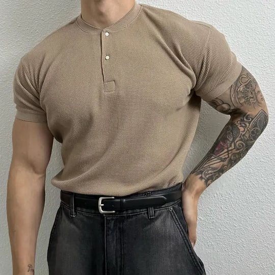 Person wearing a beige short-sleeve shirt and black pants against a plain background