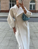 Person wearing a long white coat on a city street.