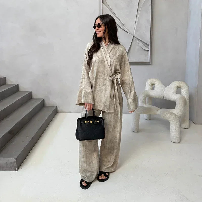 Woman in a beige outfit holding a black handbag in a modern interior setting.