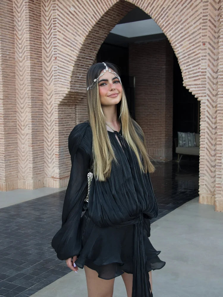 Woman in a black dress standing in front of a brick archway.