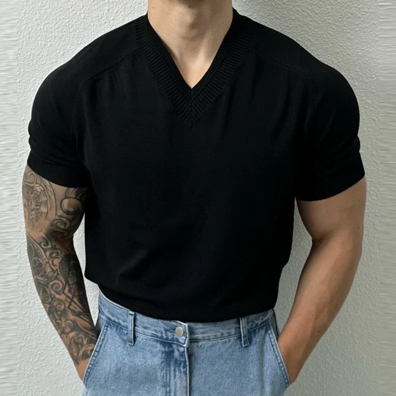Person wearing a black short-sleeve sweater and light blue jeans against a neutral background