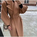 Person wearing a long brown coat on a snowy street.