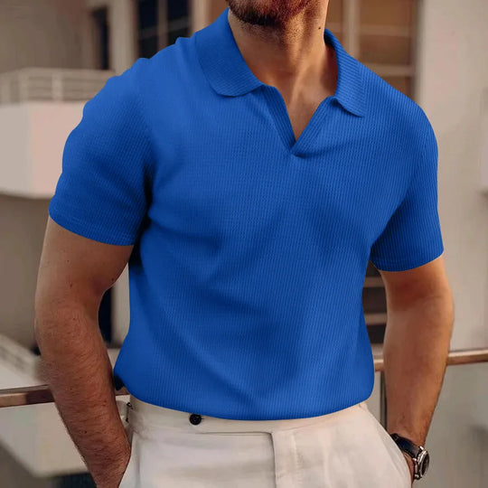 Man wearing a blue polo shirt with a blurred indoor background