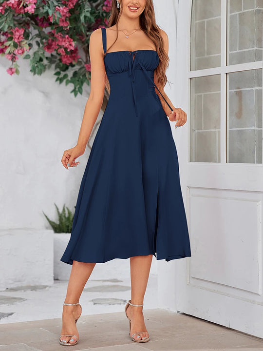 Woman wearing a navy blue dress standing outdoors with a white door and pink flowers in the background.