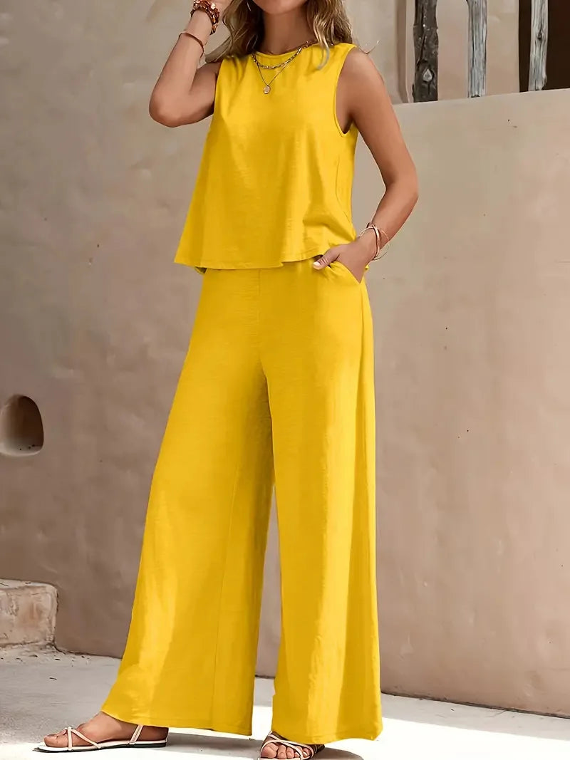 Woman wearing a yellow sleeveless top and wide-leg pants against a beige wall.