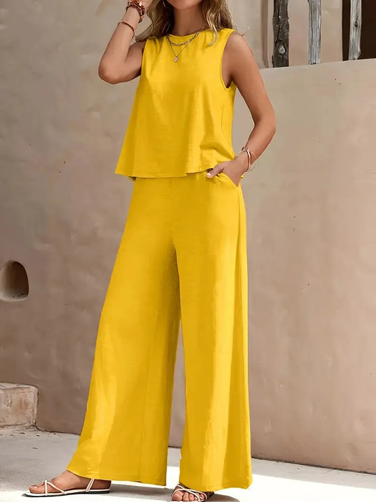 Woman wearing a yellow sleeveless top and wide-leg pants against a beige wall.