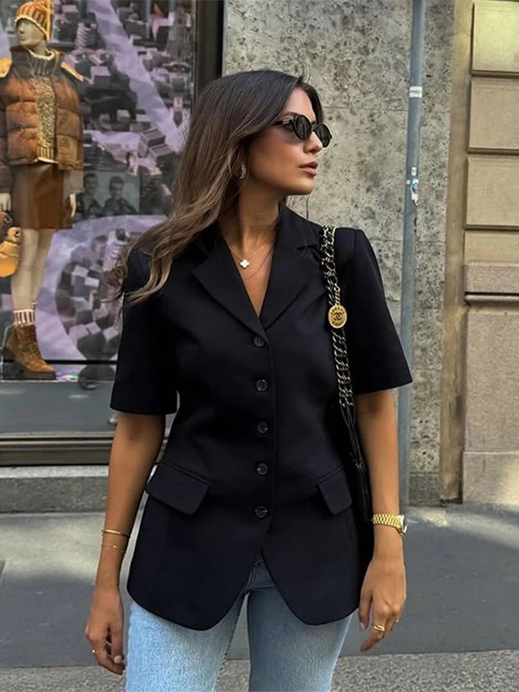 Woman wearing a black blazer and sunglasses standing on a street.