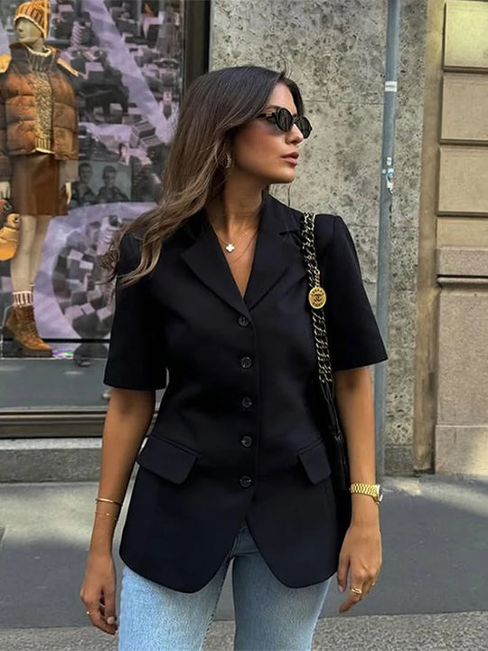 Woman wearing a black blazer and sunglasses standing on a street.