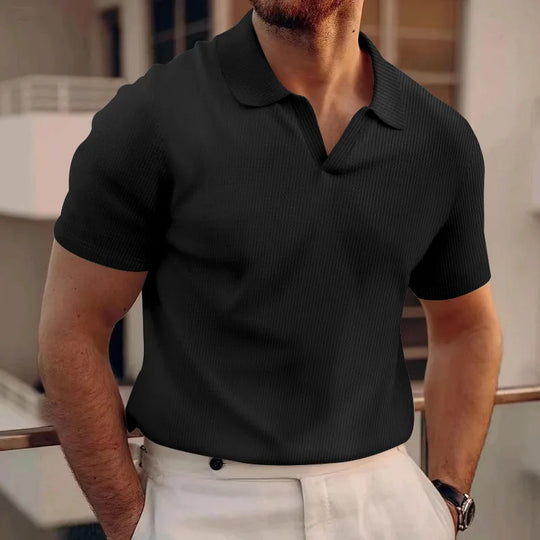 Man wearing a black polo shirt and light-colored pants indoors.