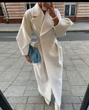 Person wearing a long white coat on a city street.