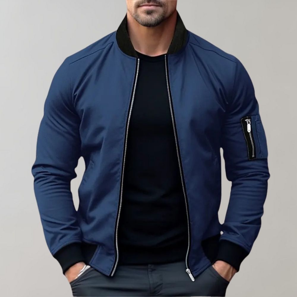 Man wearing a blue bomber jacket with black accents on a gray background