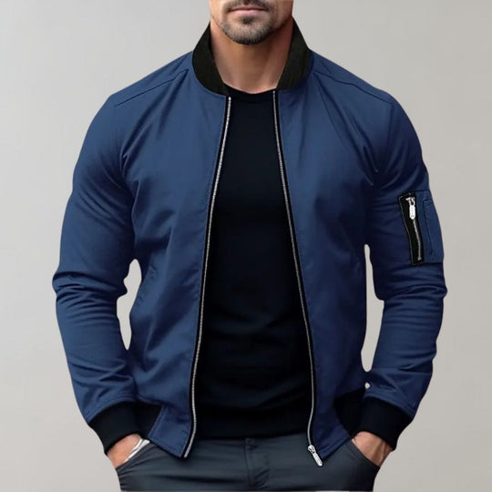 Man wearing a blue bomber jacket with black accents on a gray background