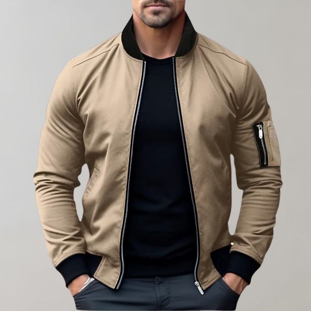 Man wearing a beige bomber jacket with black trim on a gray background