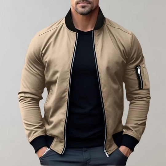 Man wearing a beige bomber jacket with black trim on a gray background