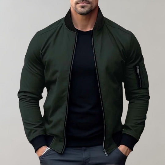 Man wearing a dark green bomber jacket over a black shirt on a gray background